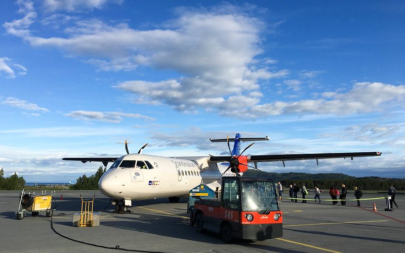 A White Color Plane with Passengers Boarding on it at Trondheim Airport.