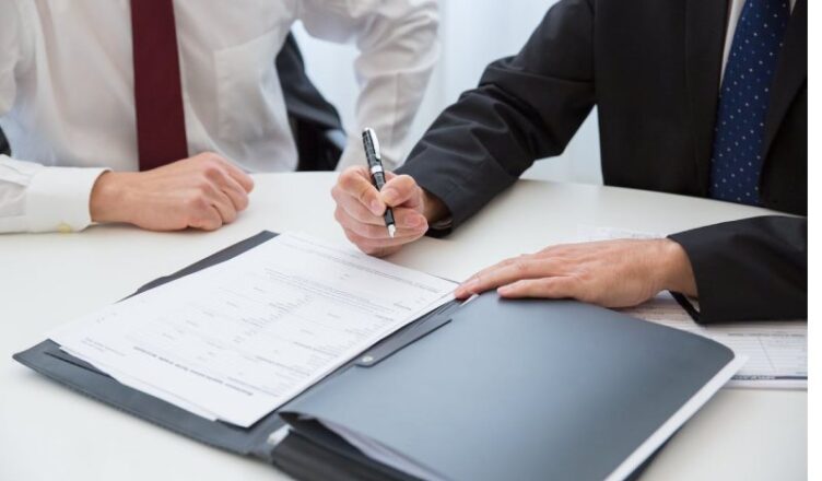 A Person in Black Suit Holding a Pen Near the Documents on the Table