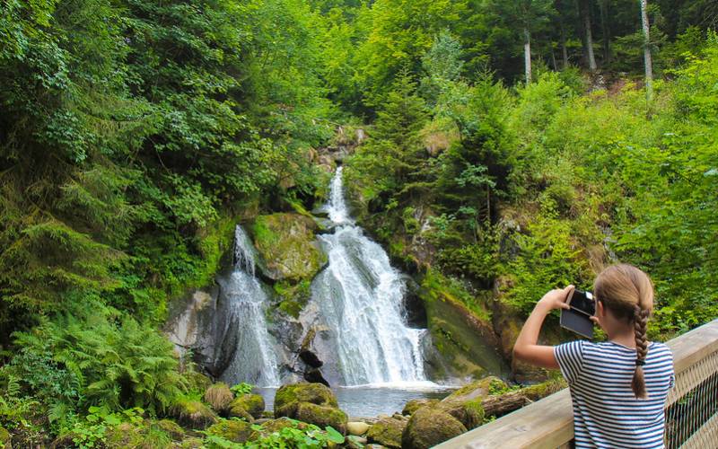 A girl clicking pictures of waterfall at black forest in Germany.