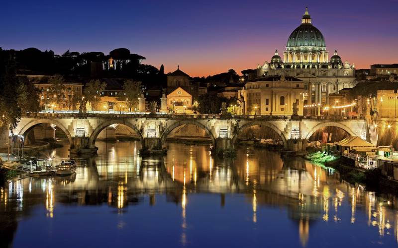 Beautiful concrete building in Rome shining with lights near a river.