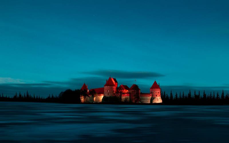 Red color castle under grey clouds at night in Lithuania.