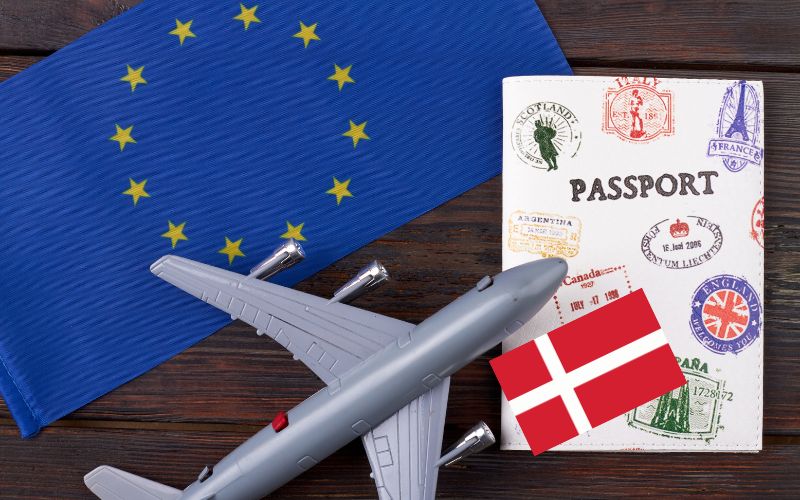 Schengen and Denmark flags, airplane model, and passport on a table